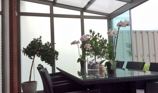 Schuifbare veranda tuinkamer met matglas zijwand en glazen schuifwanden.
